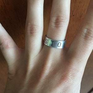 Peut inclure: Une bague en argent avec le mot "STOM" gravé dessus.