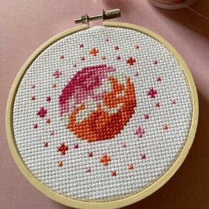 Puede incluir: Un círculo degradado rosa y naranja con estrellas blancas sobre un fondo blanco, enmarcado en un aro de madera.