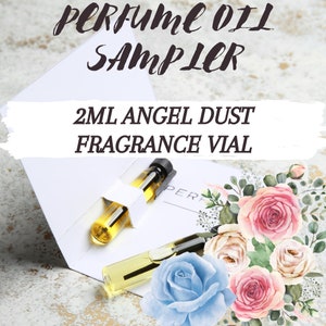May include: A 2 ml glass vial of Angel Dust fragrance oil in a white cardboard sampler with a floral design. The sampler is open and the vial is visible. The text "PERFUME OIL SAMPLER" and "2 ML ANGEL DUST FRAGRANCE VIAL" is printed on the sampler.