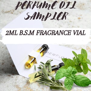 May include: Two small glass vials with a yellow liquid inside, labeled "PERFUME OIL SAMPLER 2ML B.S.M FRAGRANCE VIAL". The vials are in a white cardboard box with green leaves of basil, mint, and sage.