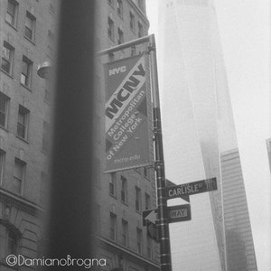 Può includere: Una foto in bianco e nero di un edificio alto con un cartello per il Metropolitan College of New York, NYC, su un angolo di strada. Il cartello è su un palo con un cartello stradale che dice "Carlisle St. Way".