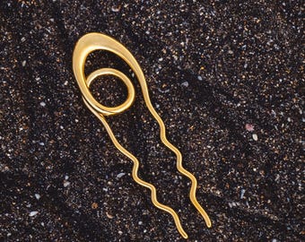 May include: A gold hair comb with a wavy design and a circular detail at the top.
