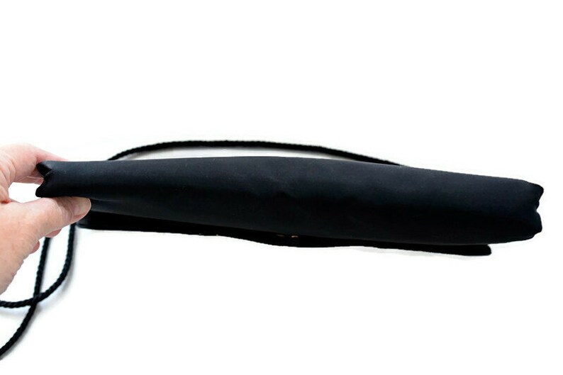 Puede incluir: Bolso de mano de sat&eacute;n negro con una correa de hombro de cuerda negra. El bolso es rectangular y parece estar vac&iacute;o. El fondo es blanco.