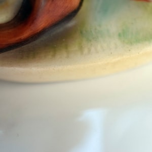 Puede incluir: Primer plano de una figura de cer&aacute;mica con una base de color crema. La figura presenta un remolino de naranja y marr&oacute;n, con acentos verdes y naranjas. La base tiene una superficie ligeramente texturizada.