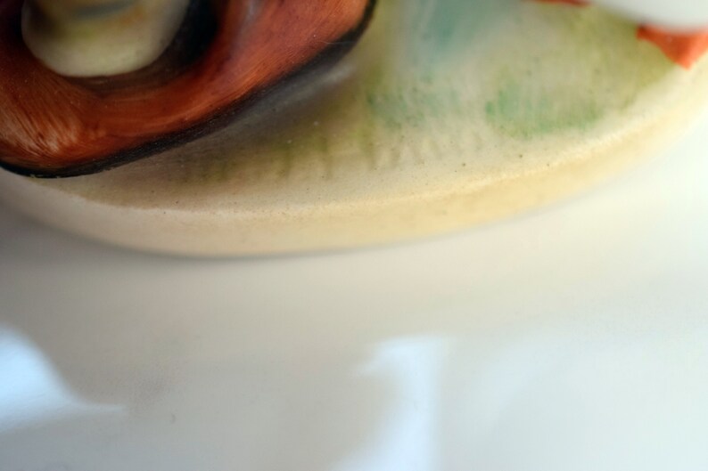 Puede incluir: Primer plano de una figura de cer&aacute;mica con una base de color crema. La figura presenta un remolino de naranja y marr&oacute;n, con acentos verdes y naranjas. La base tiene una superficie ligeramente texturizada.