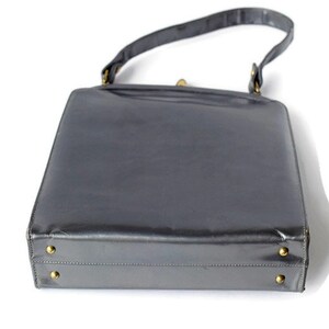 Puede incluir: Un bolso rectangular vintage de color gris oscuro. El bolso tiene un acabado brillante, un asa superior y herrajes dorados. La base del bolso presenta cuatro peque&ntilde;os pies dorados.