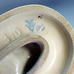 Puede incluir: Primer plano de la parte inferior de un objeto de cer&aacute;mica color crema. El borde tiene un borde moteado de color canela. Las marcas azules incluyen un dise&ntilde;o floral, el n&uacute;mero "2" y el n&uacute;mero "9". La palabra "BAVO" tambi&eacute;n es visible.