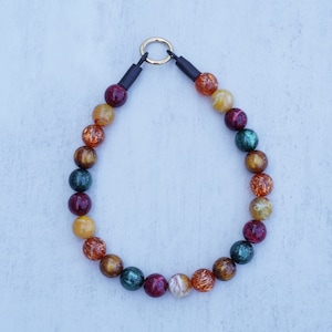 Op de afbeelding: Een ketting gemaakt van gekleurde glazen kralen met een gouden metalen sluiting. De kralen zijn een mix van rood, oranje, geel en groen.