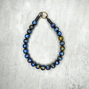 Op de afbeelding: Een blauwe en gouden kralenketting met een zwart koord en een gouden sluiting.