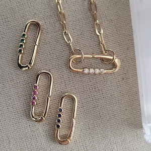 May include: A set of gold-toned chain links and four different colored charm clasps. The clasps are oval-shaped and have a row of small gemstones. The colors of the gemstones are green, pink, blue, and clear.