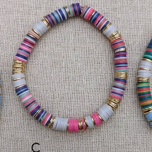 May include: A colorful beaded bracelet with gold accents. The beads are layered with stripes of pink, blue, white, and gray.