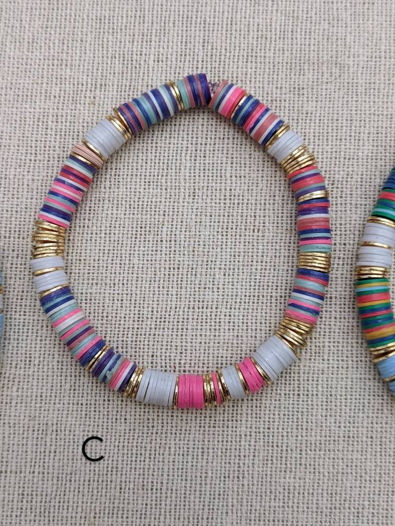 May include: A colorful beaded bracelet with gold accents. The beads are layered with stripes of pink, blue, white, and gray.