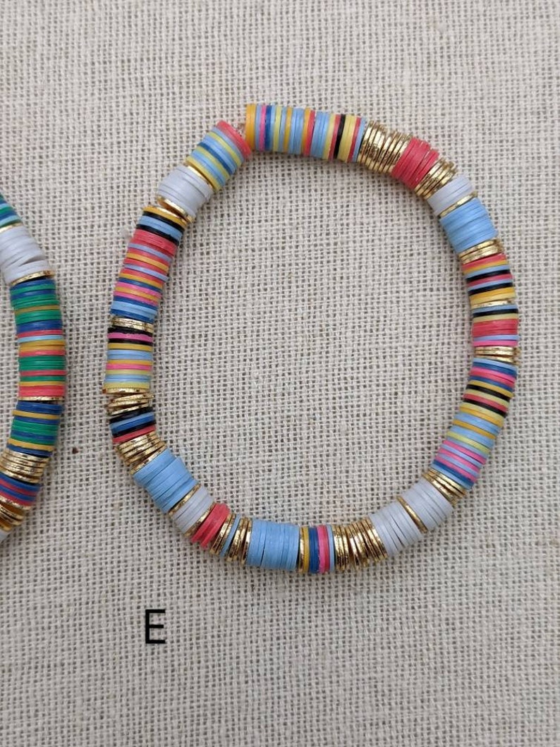May include: A colorful bracelet made of stacked, round, flat beads with gold accents. The beads are in shades of blue, pink, yellow, green, and white.