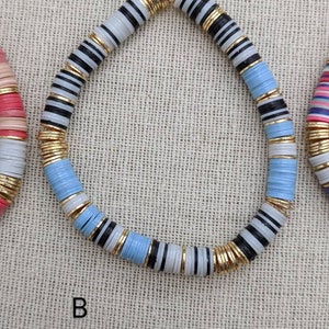 May include: A blue, white, and black beaded necklace with gold accents. The necklace is made of round, flat beads with a striped pattern.