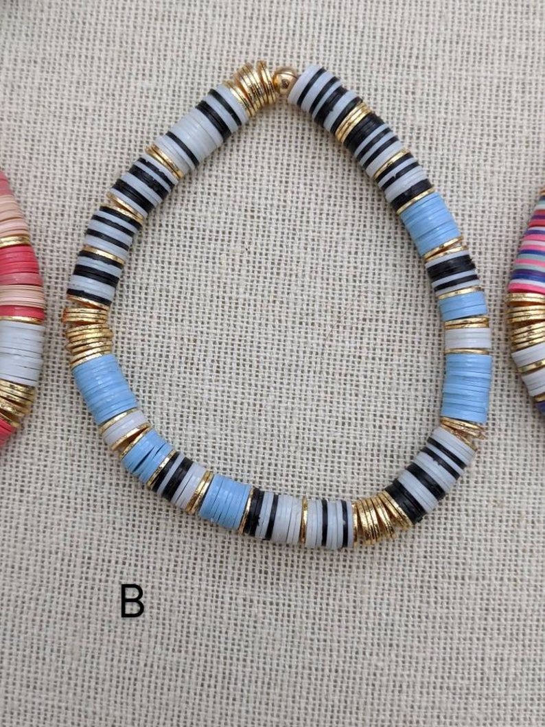 May include: A blue, white, and black beaded necklace with gold accents. The necklace is made of round, flat beads with a striped pattern.