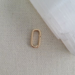 May include: A gold-toned, rectangular-shaped jewelry connector with a rope-like design.