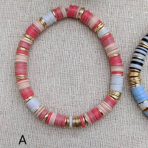 May include: A pink, white, and gold beaded bracelet. The beads are stacked and have a slightly rounded shape.