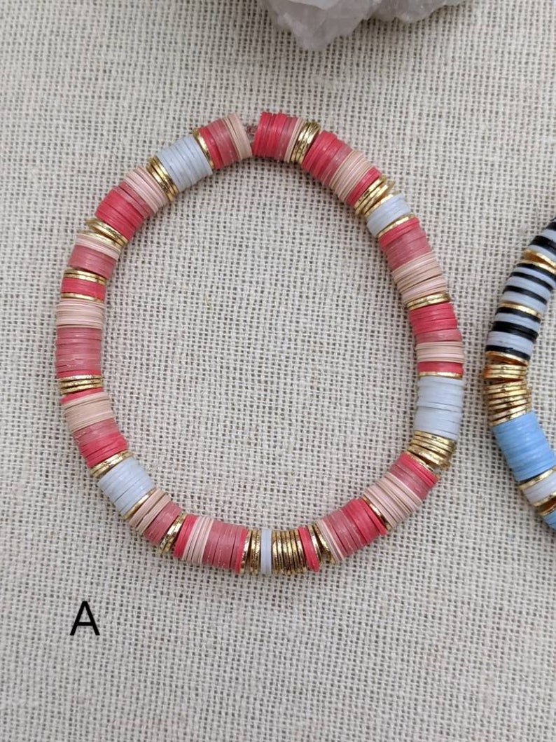 May include: A pink, white, and gold beaded bracelet. The beads are stacked and have a slightly rounded shape.