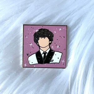 May include: A pink enamel pin with a black outline of a person with black hair wearing a white shirt and a black tie. The background is a pink and white speckled design with white stars.