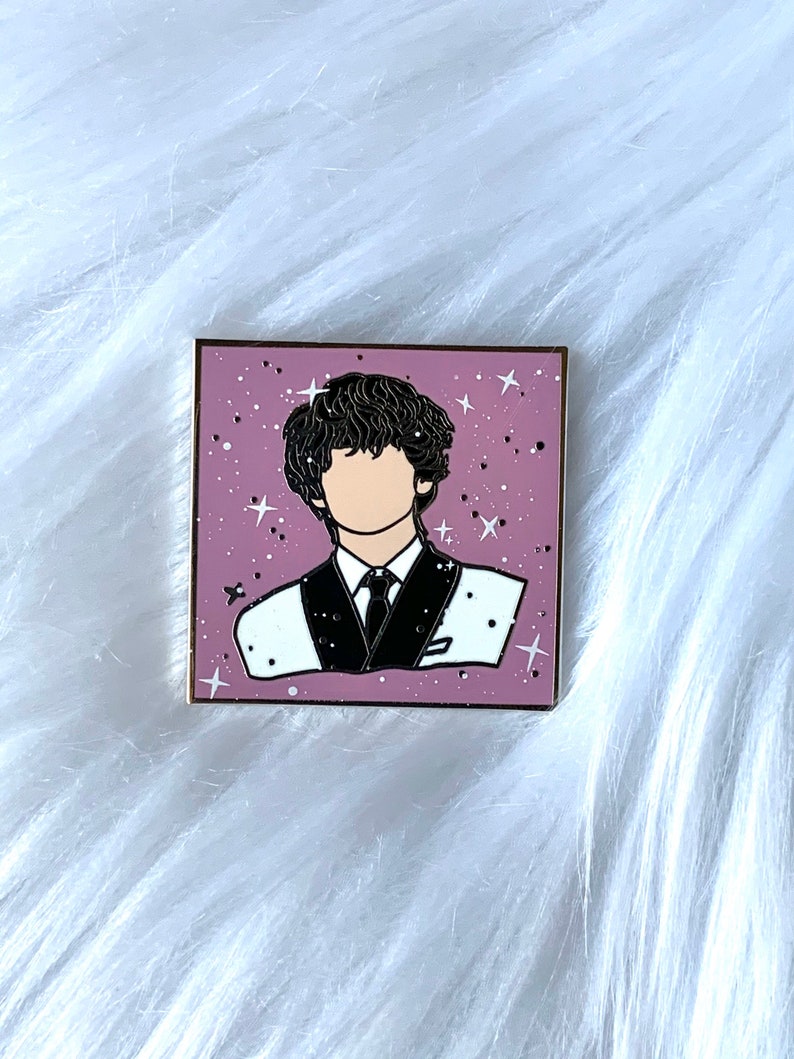 May include: A pink enamel pin with a black outline of a person with black hair wearing a white shirt and a black tie. The background is a pink and white speckled design with white stars.