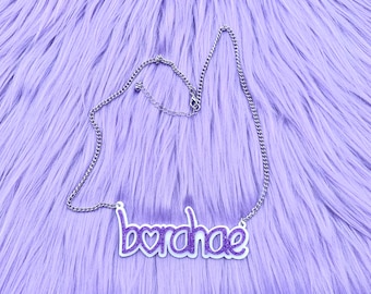 May include: A silver chain necklace with a purple glitter pendant that says "b*r*d*h*a*e" with a heart in place of the "o".