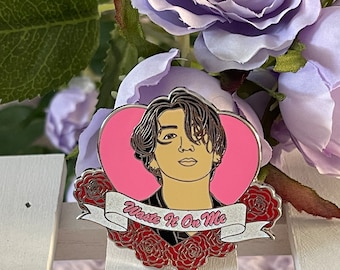 Puede incluir: Un pin de esmalte plateado con un retrato de dibujos animados de una persona con cabello oscuro en un marco en forma de corazón. El corazón es rosa y la persona lleva una camisa con estampado blanco y negro. El pin tiene una pancarta blanca con el texto "Waste It On Me" en letras negras. El pin está rodeado de rosas rojas.