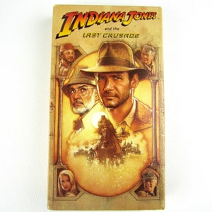May include: A vintage VHS tape cover featuring a colorful illustration of Indiana Jones and his father, with the title "Indiana Jones and the Last Crusade" in bold, white text.