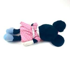 May include: A plush toy of a cartoon mouse wearing a pink polka dot dress and black shoes. The mouse has black ears and a black nose.