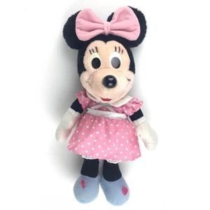 May include: A plush toy of Minnie Mouse wearing a pink dress with white polka dots and a pink bow. She has black eyes and a black nose.