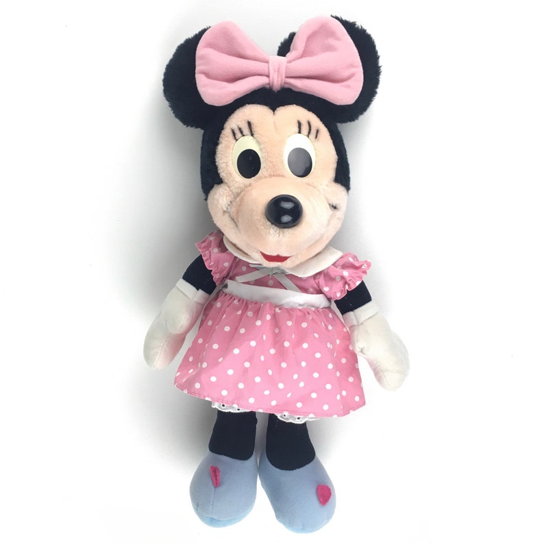 May include: A plush toy of Minnie Mouse wearing a pink dress with white polka dots and a pink bow. She has black eyes and a black nose.