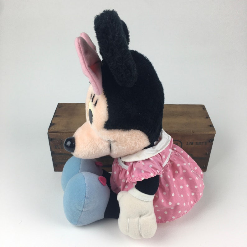 May include: A plush Minnie Mouse toy wearing a pink polka dot dress with a white collar and blue shoes. She has black fur, pink ears, and a white face.