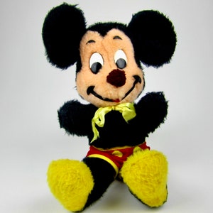 Puede incluir: Un juguete de peluche Mickey Mouse negro y marr&oacute;n con zapatos amarillos y una pajarita roja y amarilla.