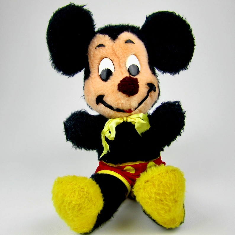 Puede incluir: Un juguete de peluche Mickey Mouse negro y marr&oacute;n con zapatos amarillos y una pajarita roja y amarilla.
