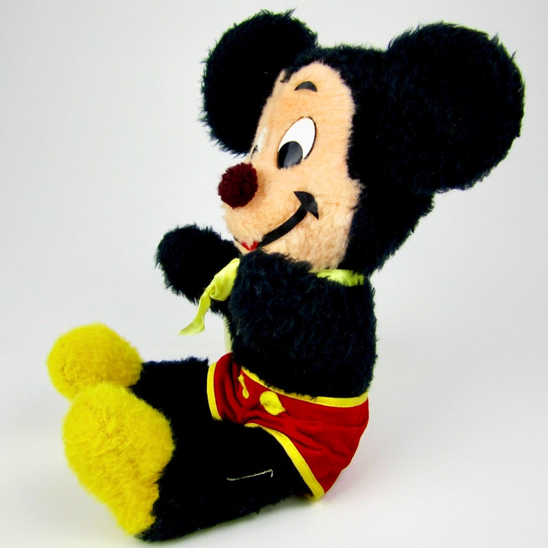 Puede incluir: Un juguete de peluche vintage de Mickey Mouse con pelaje negro, zapatos amarillos y pantalones cortos rojos y amarillos. El juguete tiene una cara sonriente con ojos negros y una nariz roja.