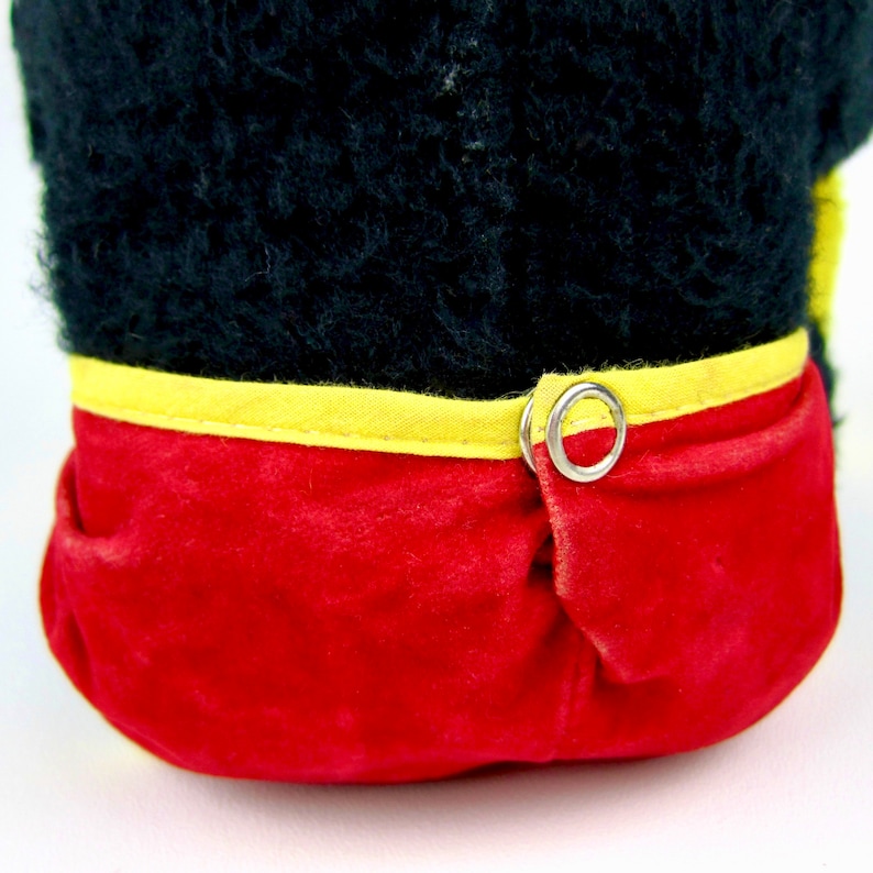 Puede incluir: Juguete de peluche negro con ribete rojo y amarillo. El juguete tiene un anillo de metal en la parte posterior.