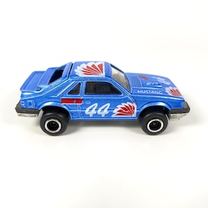 Puede incluir: Coche de juguete azul con calcomanías de carreras rojas y blancas. El coche tiene el número 44 en el lateral y las palabras "SVO Mustang" en la parte trasera.