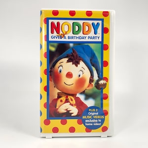 May include: A Noddy VHS tape with a yellow cover featuring red polka dots. The cover displays the title "NODDY GIVES A BIRTHDAY PARTY" and an image of Noddy wearing a blue hat. Additional text indicates "PLUS 2 Original MUSIC VIDEOS exclusive to home video!"