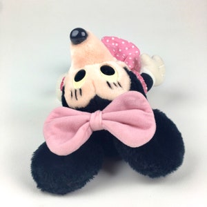 May include: A plush black and pink Minnie Mouse toy with a pink bow and a polka dot dress.