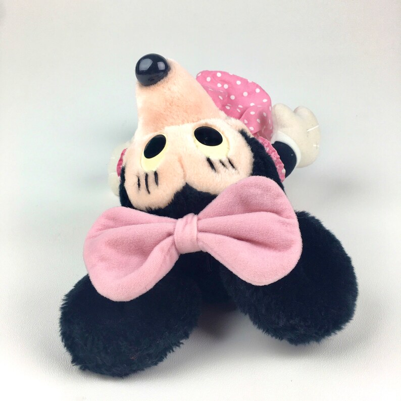 May include: A plush black and pink Minnie Mouse toy with a pink bow and a polka dot dress.
