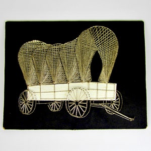 May include: A black framed wall art piece featuring a white string art design of a covered wagon with wheels. The wagon is made of string and is set against a black background.