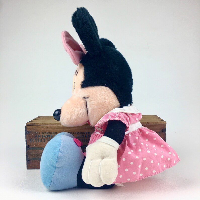 May include: A plush Minnie Mouse toy wearing a pink dress with white polka dots and a blue bow. The toy has black fur and a pink bow on its head.