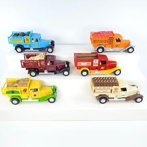 May include: A collection of six toy trucks with different colored bodies and cargo beds. The trucks are made of plastic and have detailed features, including wheels, headlights, and cargo. The cargo beds are filled with various items, such as bricks, logs, and coffee beans.