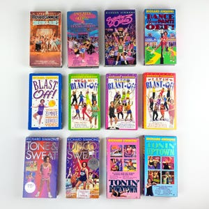 May include: A selection of vintage Richard Simmons workout VHS tapes. The tapes have vibrant covers with images of Simmons and exercise routines. Titles include "Sweatin' to the Oldies," "Blast Off!," and "Dance Your Pants Off!"