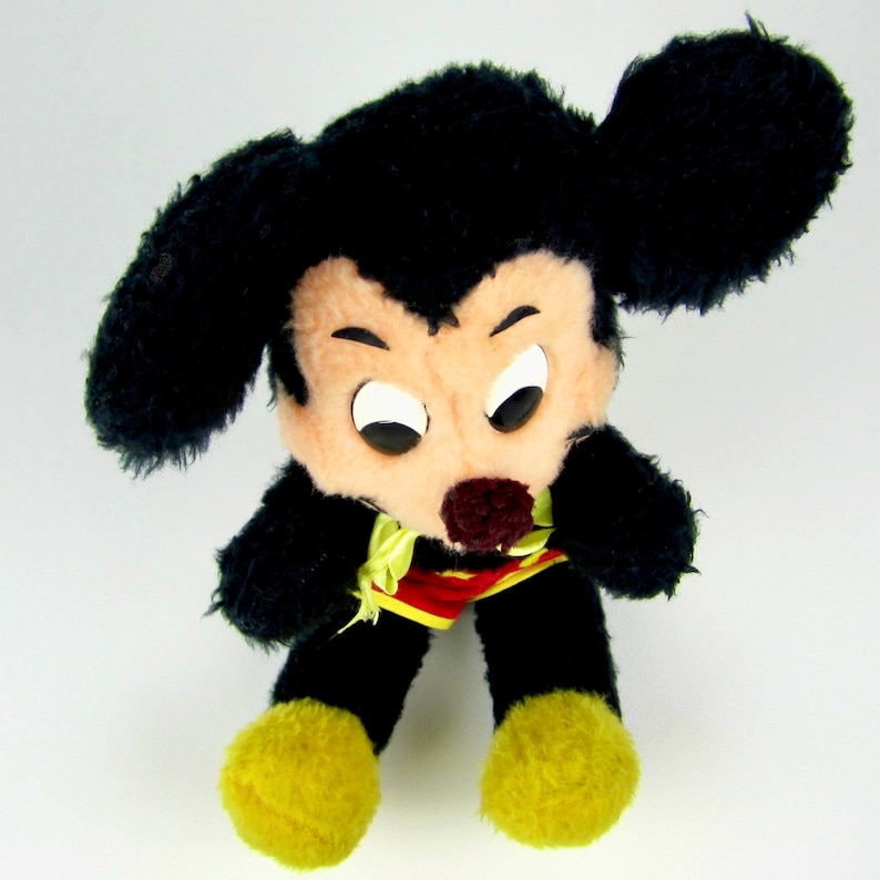 Puede incluir: Un juguete de peluche Mickey Mouse negro con una camisa hawaiana roja y amarilla. El juguete tiene una expresi&oacute;n gru&ntilde;ona con ojos grandes y el ce&ntilde;o fruncido.