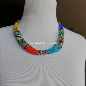 Puede incluir: Un collar de cuentas de varios hilos con una paleta de colores vibrantes. El collar presenta hilos de cuentas rojas, turquesas, amarillas y azules, con una sección estampada en el centro. El texto "everythingzulu.com" es visible.