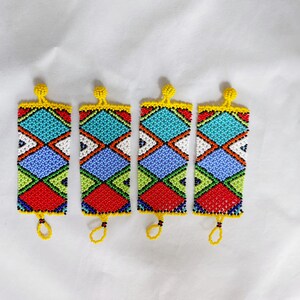 May include: Four beaded rectangular ornaments with a geometric pattern. The ornaments feature a vibrant mix of colors, including red, blue, green, white, and yellow. Each has a loop at the bottom and a beaded top.