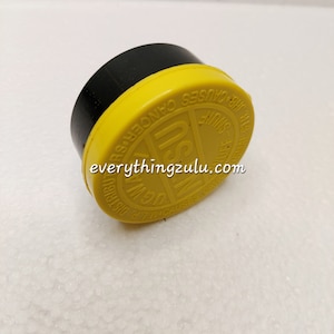 以下が含まれることがあります： 「EVERYTHINGZULU.com」の文字とその他の文字が入った、黒と黄色のプラスチック製の物体。この物体は、円形の黄色の上面と黒色の基部を持っています。黄色の上面には「CAUSES CANCER」と「SHUFF」の文字が入っています。
