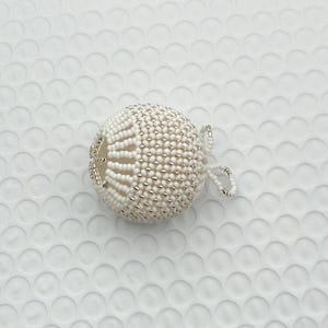 May include: A white beaded sphere ornament with a loop for hanging. The ornament is covered in small white beads with silver-colored accents. The sphere has a decorative open design on one side.