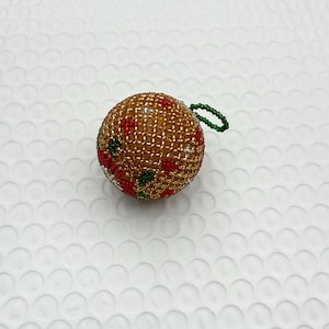 May include: A beaded Christmas ornament. The ornament is a sphere, primarily gold with red and green accents. It has a green loop for hanging.