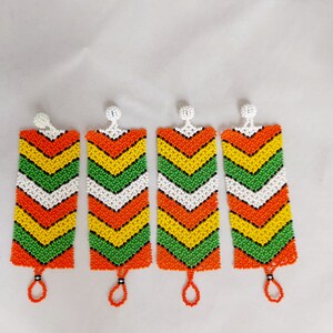 May include: Four beaded earrings with a rectangular shape and a chevron pattern. The earrings feature a color scheme of orange, yellow, green, white, and black beads. Each earring has a small loop at the bottom and a white bead at the top.